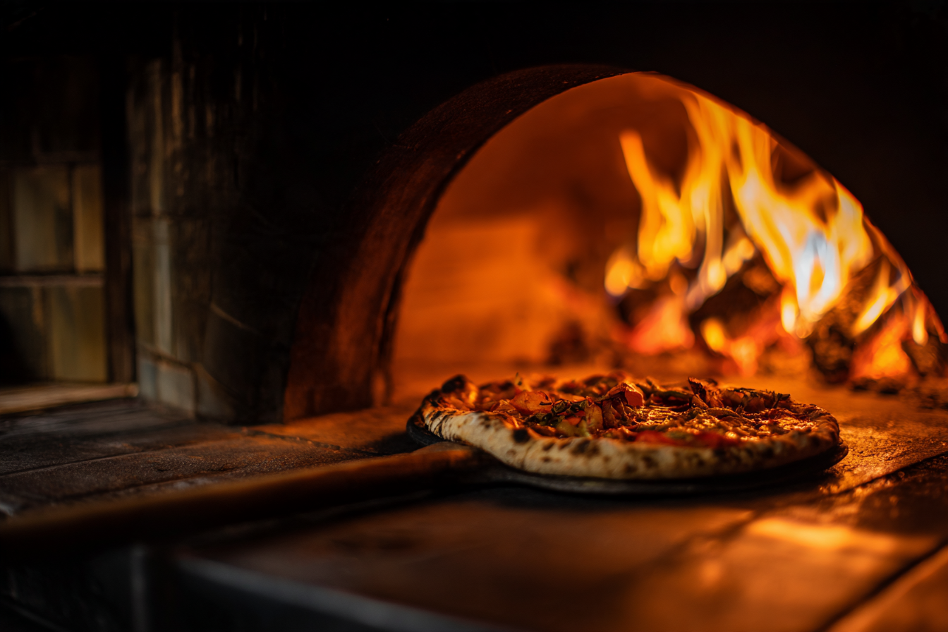 A pizza sliding into the wood-fired oven, flames behind