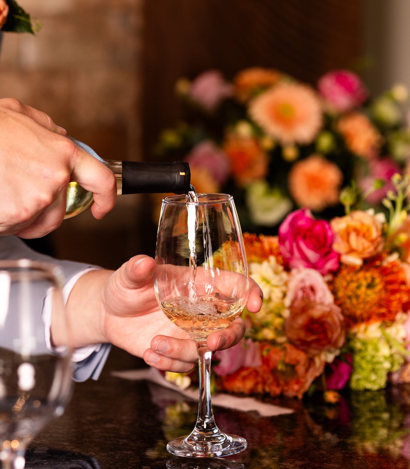 A glass of white wine being poured beside wedding flowers